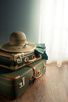 Vintage suitcase with straw hat on the floor next to a window.