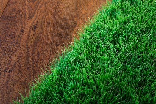 Artificial lush grass close-up on wooden hardwood floor.