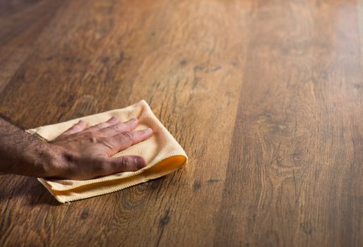 Male hand cleaning and rubbing an hardwood floor with a microfiber cloth.