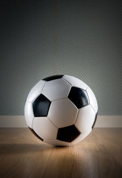 Soccer ball on hardwood floor and vintage wallpaper on background.