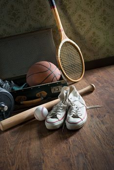 Vintage suitcase with sports equipment on wooden floor with canvas shoes on foreground.