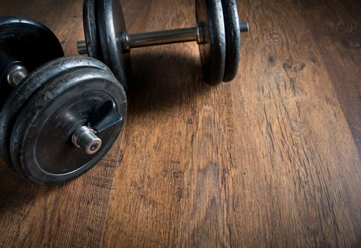 Black barbell weights on dark hardwood floor, weightlifting training concept.