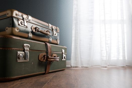 Pile of vintage suitcases next to a window on hardwood floor.