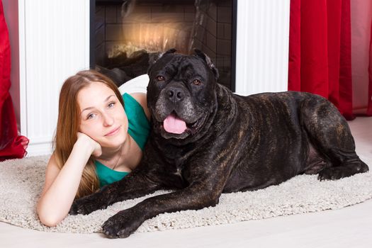 Girl lying near the fireplace with a dog Cane Corso. Horizontal framing