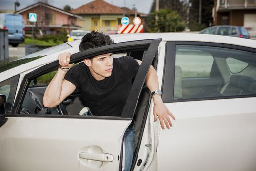Young attractive man getting out of white car, opening the door