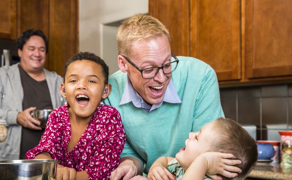 Same sex couple with two adorable children laughing in kitchen