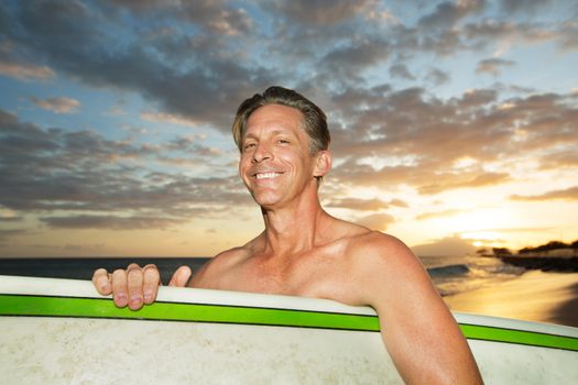 One adult Caucasian surfer with surfboard at sunset