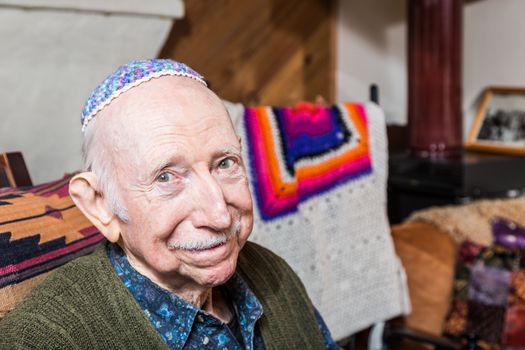 Elderly gentleman in green vest and yarmulke seated in his livingroom