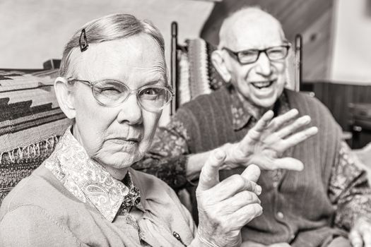 Toned image of angry old couple sitting in living room woman pointing