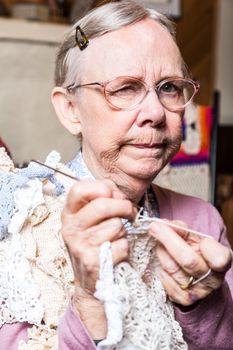 Suspicious old woman in pink sweater crocheting at home