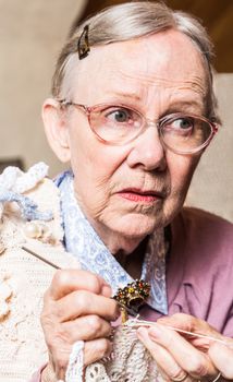 Old woman crocheting with worried expression