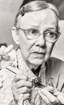 Toned image of old woman crocheting with worried expression