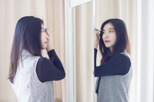 Asian portrait beautiful woman making make-up with brush on eyebrow near mirror
