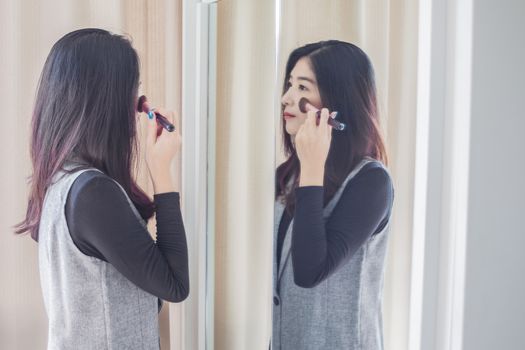 Asian portrait beautiful woman making make-up with brush on face near mirror