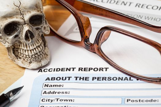 Accident report application form and human skull on brown envelope and eyeglass, business insurance and risk concept; document is mock-up