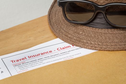 Travel Insurance Claim application form and hat with eyeglass on brown envelope, business insurance and risk concept; document is mock-up