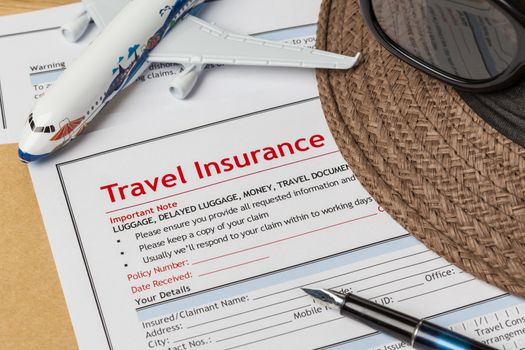 Travel Insurance Claim application form and hat with eyeglass and pen on brown envelope, business insurance and risk concept; document and plane is mock-up