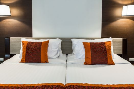 Red pillow on bedroom with white bedsheet and lamp light on