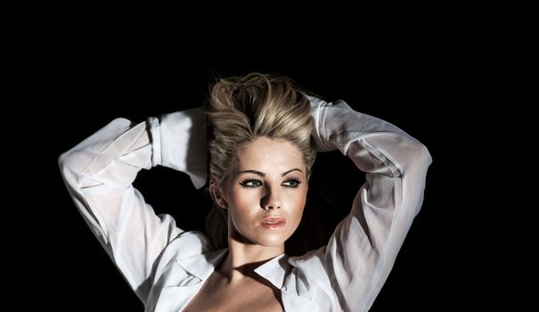 pretty blonde woman with arms behind her head on black background