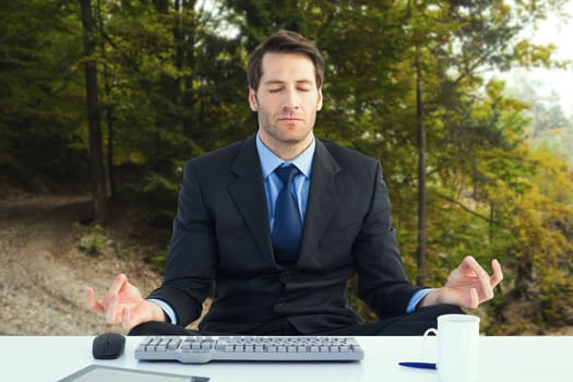 Calm businessman sitting in lotus pose against tarmac curved country road in forest