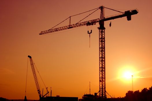 Industrial landscape. Construction cranes against sunset.