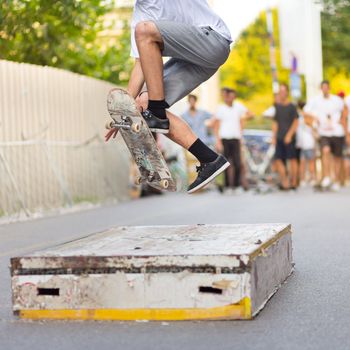Young skateboarder skateboarding on an object in street. Skateboarding legs doing trick ollie at skatepark. Group of friends cheering in the background.