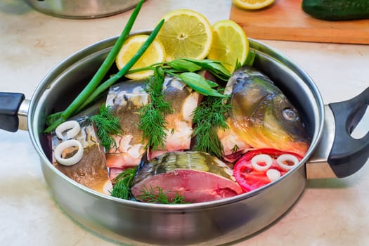 In a large skillet, stainless steel is chopped fish and ingredients for cooking: vegetables, lemon, onion, dill.