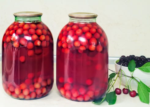 Home canning: large glass cylinders with cherry compote, sealed with metal caps.