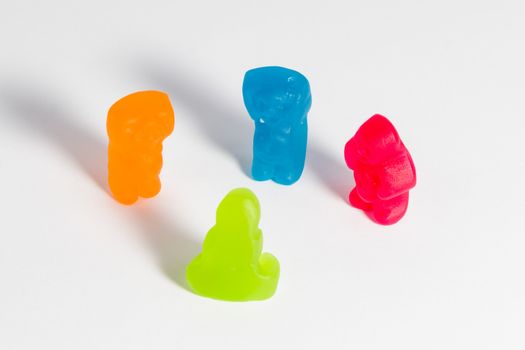 Red, blue, orange and green jelly babies in discussion, on a white background.