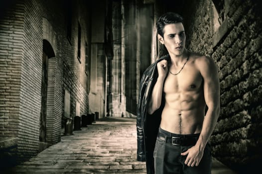 Portrait of a Young Vampire Man in an Open Black Leather Jacket, Showing his Chest and Abs, Looking to Right, on Dark Background.