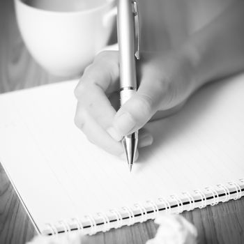 woman hand writing with pen on notebook.there are crumpled paper and coffee cup on wood table background black and white color tone style