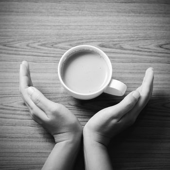 woman hand holding coffee cup on wood table background black and white color tone style