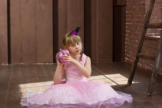 Girl 6 years old in a pink dress with a piggy bank in his hands. In Room