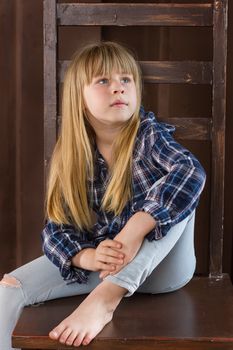 Girl 6 years old in jeans and blue shirt is sitting on a high chair in a room with brown walls