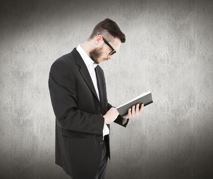 Geeky young man reading from black book against white and grey background
