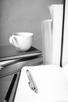 open notebook with book and coffee cup on wood background black and white color tone style