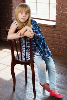 Girl 6 years old in jeans and shirt thrown sits on a chair