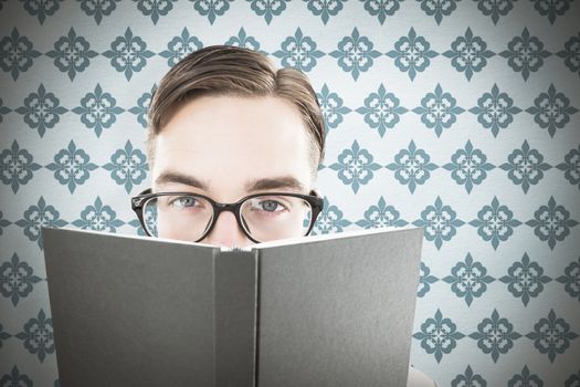 Geeky man looking over book against blue background