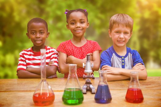 Cute pupils standing with arms crossed behind beaker against trees and meadow