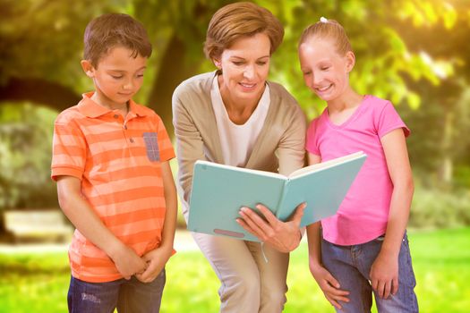 Teacher reading book with pupils at library against trees and meadow in the park