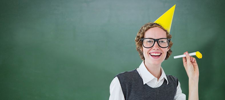 Geeky hipster in party hat with horn against green chalkboard