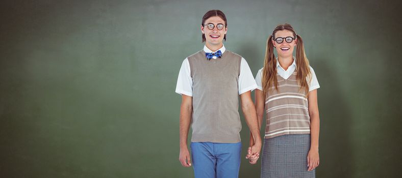 Geeky hipster couple holding hands  against green chalkboard