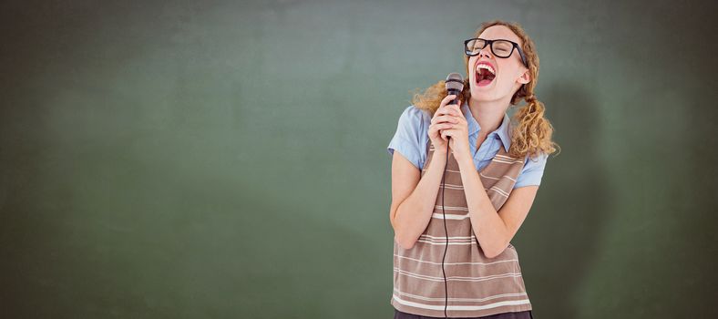 Geeky hipster woman singing into a microphone  against green chalkboard