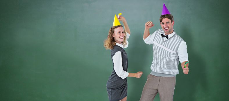 Geeky couple dancing with party hat  against green chalkboard