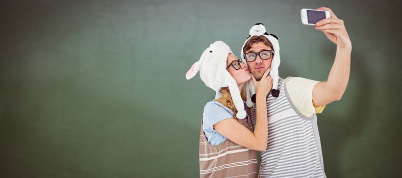 Geeky hipster couple taking selfie with smartphone against green chalkboard