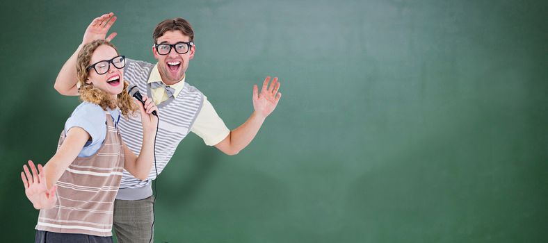 Geeky hipster couple singing into a microphone against green chalkboard