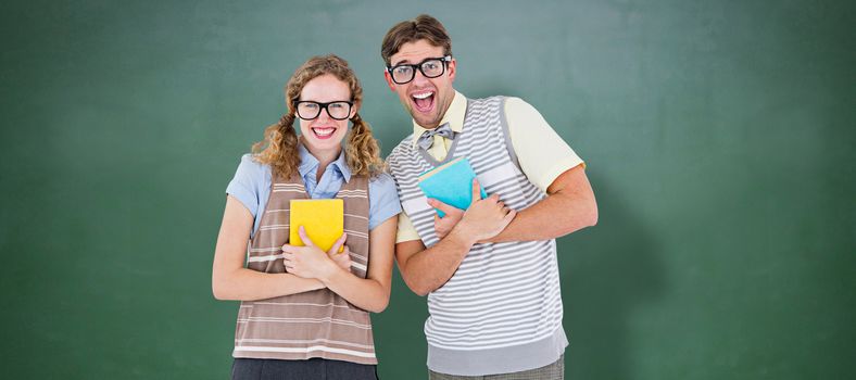 geeky hipster couple holding books and smiling at camera  against green chalkboard