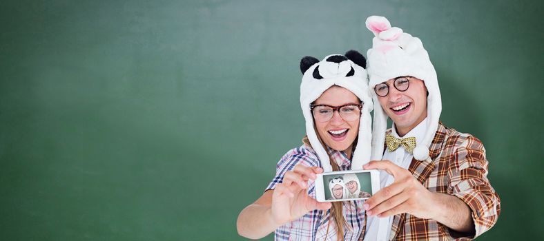 Geeky hipster couple taking selfie with smart phone  against green chalkboard