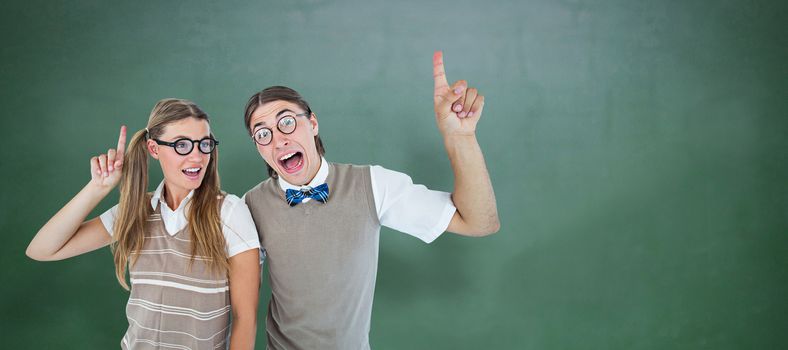 Geeky hipsters pointing against green chalkboard