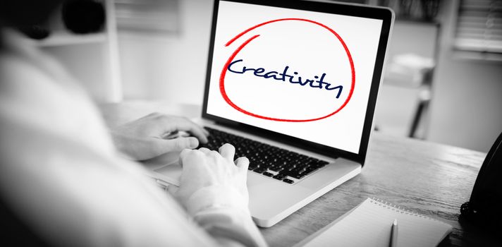 The word creativity  against businessman working on his laptop